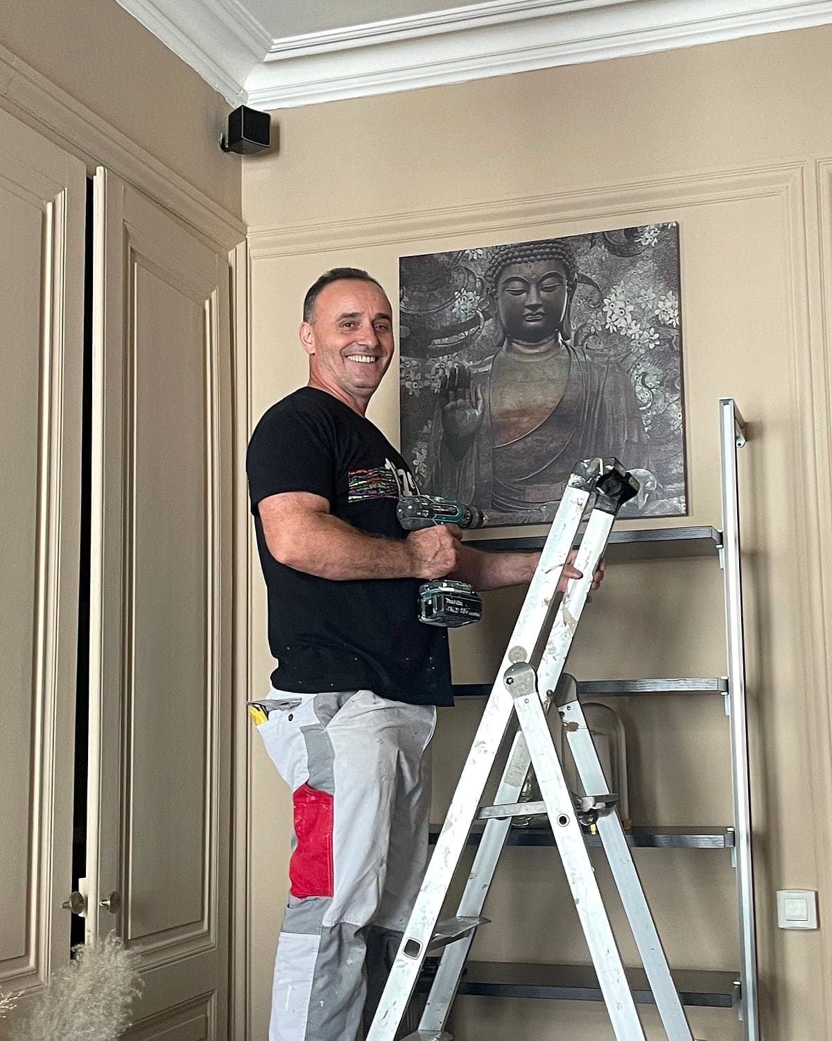 Le fondateur de BTI FINITION, souriant sur son escabeau, perceuse en main, pendant un chantier
